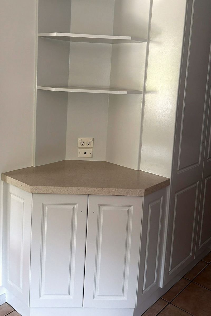 Painted corner cabinetry with open shelves and a stone benchtop