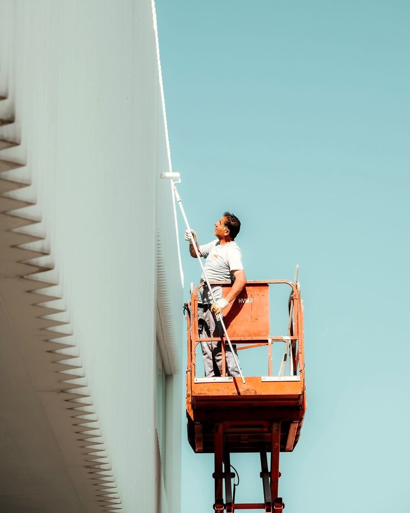 A painter on an elevated work platform rolling fresh white paint onto a contemporary facade