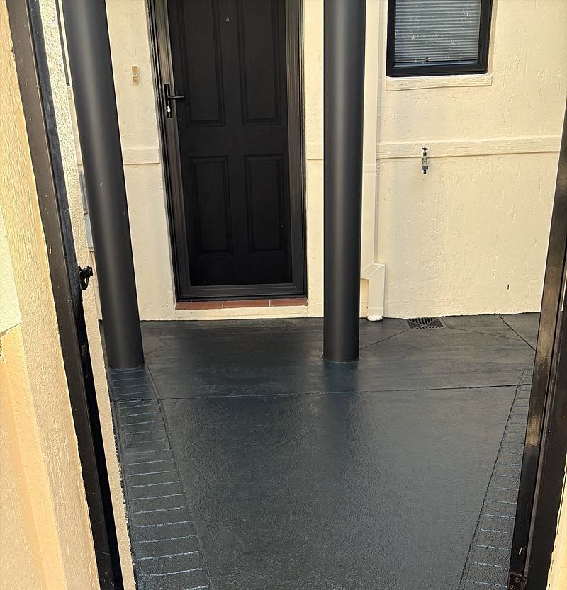 A front path coated in charcoal, running between two black posts to the front door