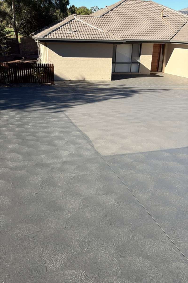 Concrete driveway with a textured grey coating, running up to a brick house