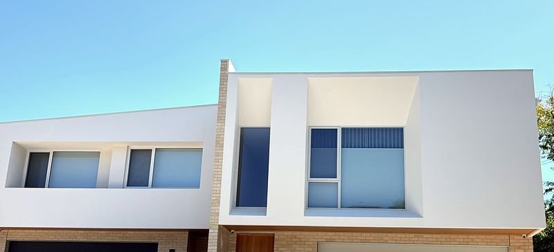 A two-storey new build with a white rendered upper storey, a face-brick pier and deep window reveals