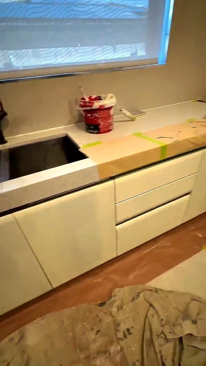 Kitchen mid-job: benchtop edges papered and taped, drop sheets over the floor