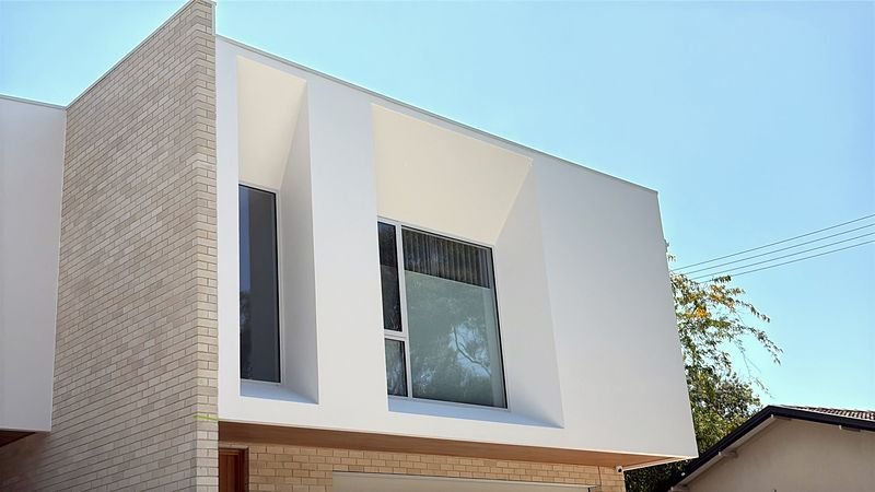 Smooth white render around a deep window reveal on a two-storey new build