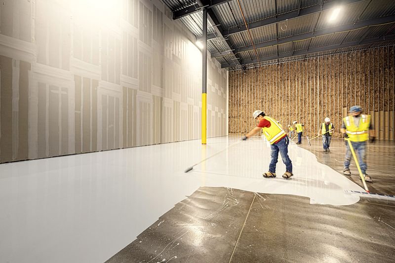 A crew rolling a protective coating across a large warehouse floor