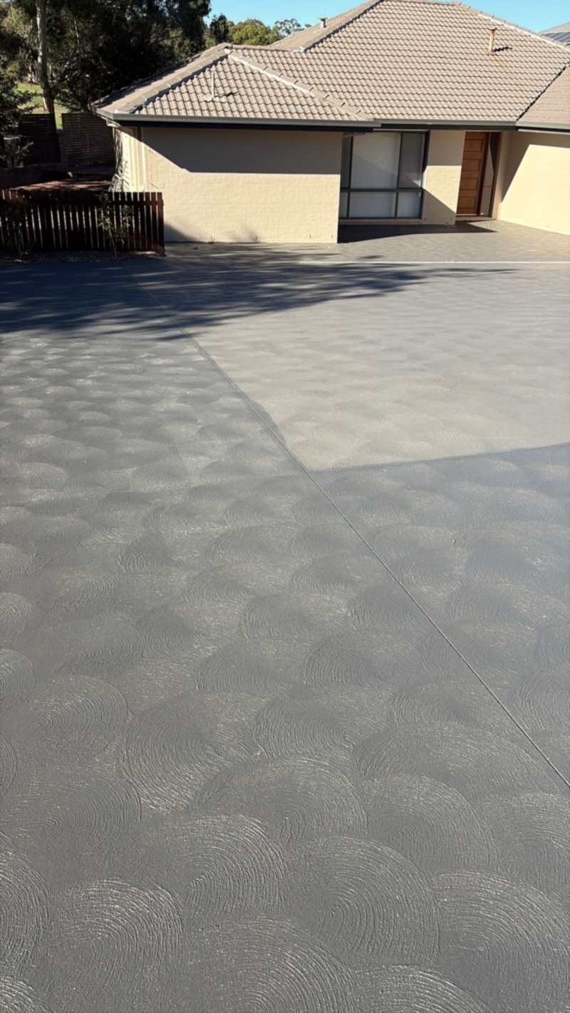 Concrete driveway with a textured grey coating, running up to a brick house